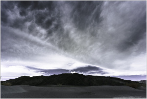 A dramatic sky looms over dark mountains in Death Valley, creating a moody atmosphere.