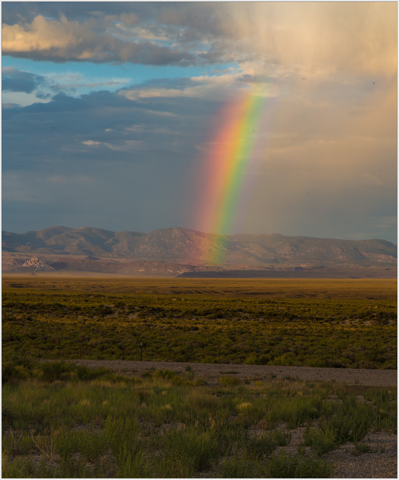 A vibrant rainbow arcs over a vast desert landscape under a dramatic sky.