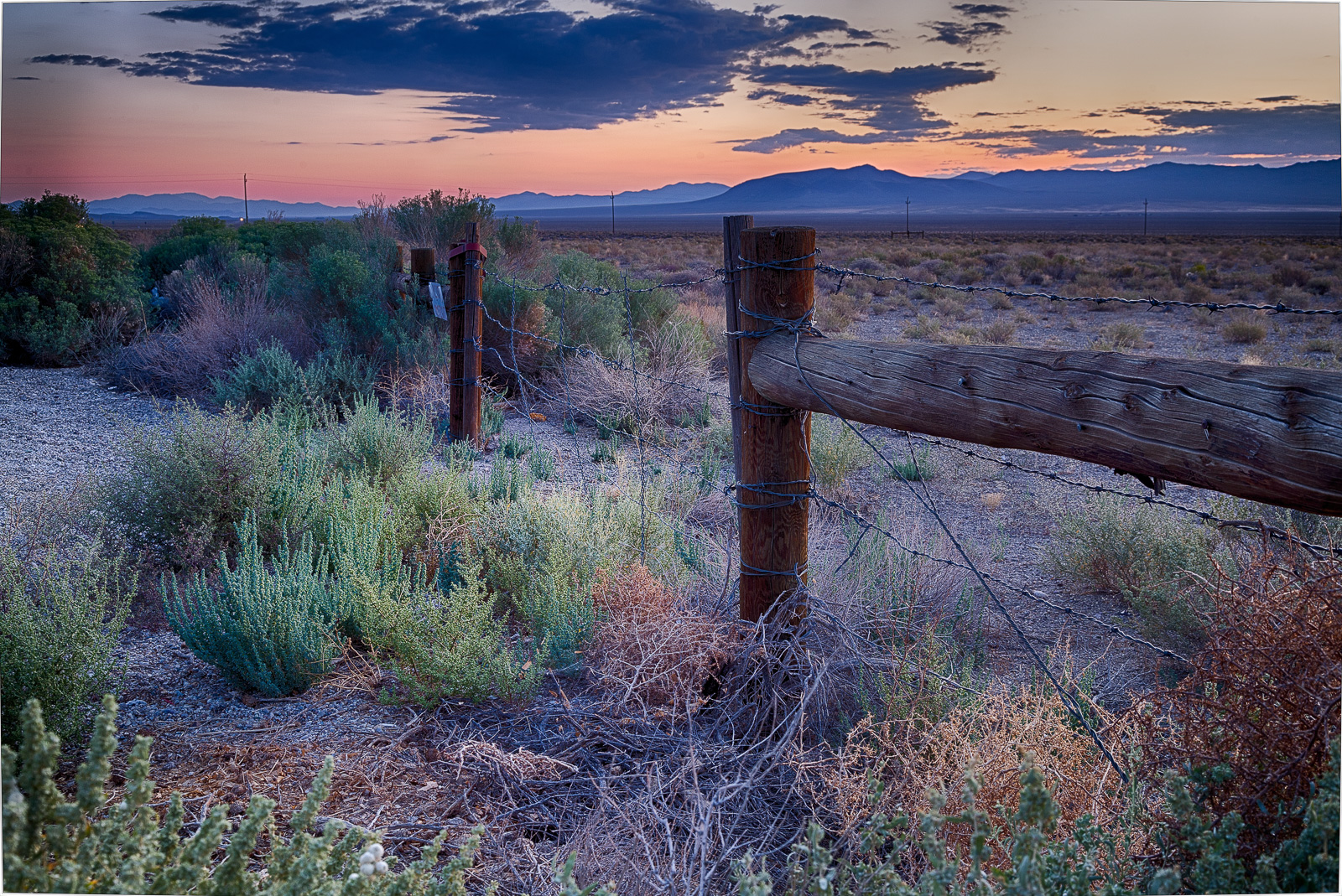 A wooden fence stands against a vast desert landscape at dusk, colors blending in the sky.