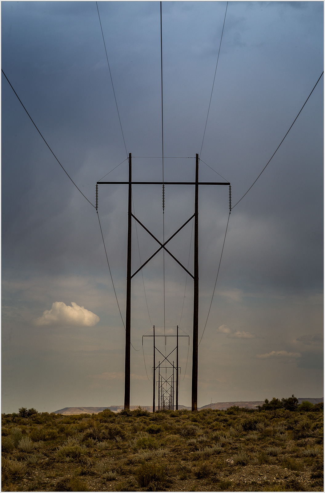 A series of towering power lines stretch across a barren landscape under a moody sky.