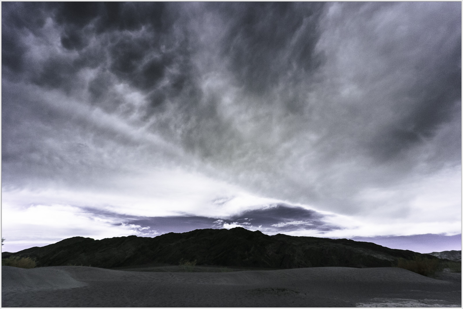 A dramatic sky looms over dark mountains in Death Valley, creating a moody atmosphere.