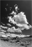 A stark desert landscape under a dramatic sky filled with clouds.