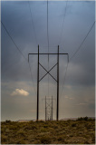 Power lines stretch into the horizon under a moody sky, surrounded by barren land.