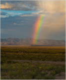 A vibrant rainbow arcs over a vast desert landscape under a dramatic sky.