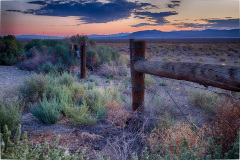 A wooden fence stands against a vast desert landscape at dusk, colors blending in the sky.
