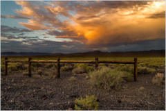 A wooden fence stretches across a barren landscape under a dramatic sky.