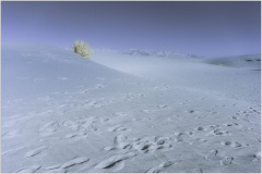 A vast, surreal desert landscape with soft, undulating dunes and a pale, ghostly formation in the distance.