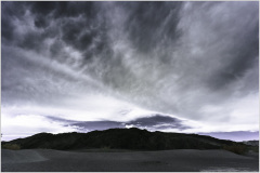 A dramatic sky looms over dark mountains in Death Valley, creating a moody atmosphere.