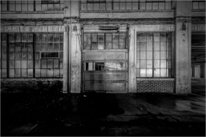 A weathered industrial entrance with large glass windows, hinting at a forgotten space.