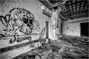 An abandoned room featuring graffiti of a skull on the wall and debris on the floor.