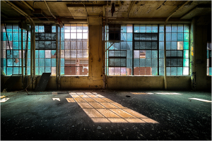 An empty room with large windows and sunlight streaming in, creating shadows on the floor.