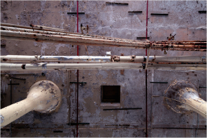 Rusty pipes intertwine like serpents on a crumbling wall, whispering forgotten tales.