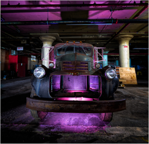 An old truck bathed in surreal purple light, surrounded by industrial shadows.