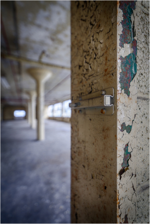 Close-up of a weathered pillar with chipped paint and a metal latch, blurred background reveals industrial space.