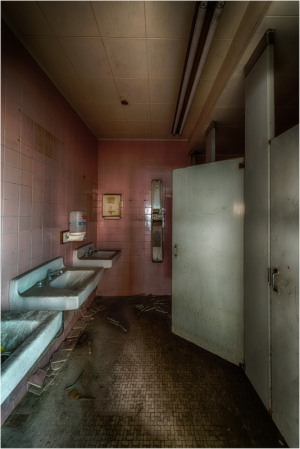 Dramatic view of a dimly lit restroom with pink tiles and grimy sinks.