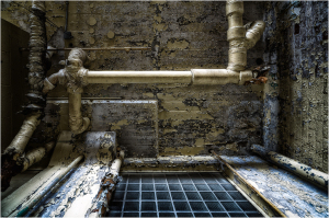 A gritty, peeling wall with old pipes and a dark grid pattern beneath.