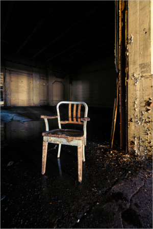 A lonely chair sits in a dimly lit, abandoned space with peeling paint.