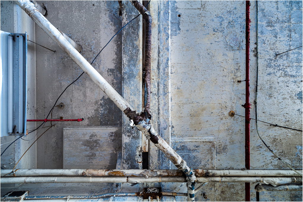 A textured, weathered wall with peeling blue paint and exposed pipes.