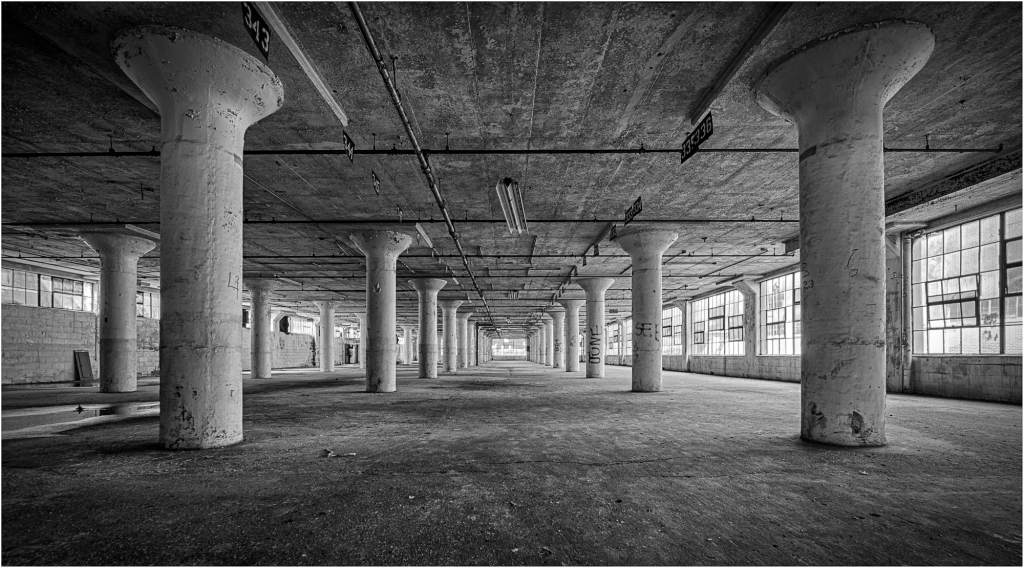 A spacious, empty warehouse with concrete pillars and large windows.