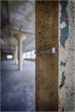 Close-up of a weathered pillar with chipped paint and a metal latch, blurred background reveals industrial space.