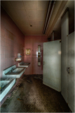 Dramatic view of a dimly lit restroom with pink tiles and grimy sinks.