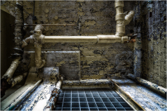 A gritty, peeling wall with old pipes and a dark grid pattern beneath.