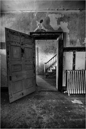 Open door reveals staircase in a dimly lit, worn interior space.