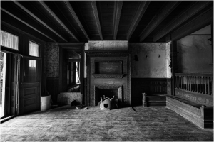An empty, dimly lit room with wooden beams and a fireplace, evoking forgotten times.