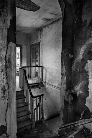 A faded staircase leads to an empty upper floor, walls peeling and worn.