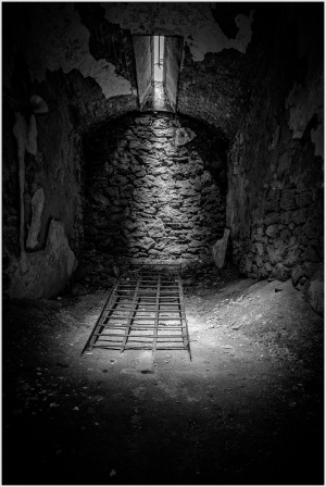 Dimly lit stone room with a barred floor and a narrow window above.