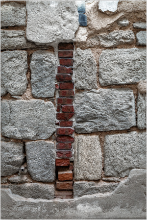 Close-up of a stone wall with a vertical strip of red bricks among gray stones.