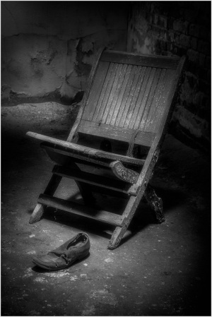 A wooden chair leaning against a wall with a single shoe on the floor nearby.