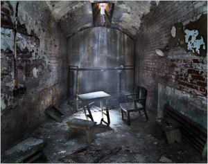 An abandoned room with a table and chair, dimly lit by a shaft of light.