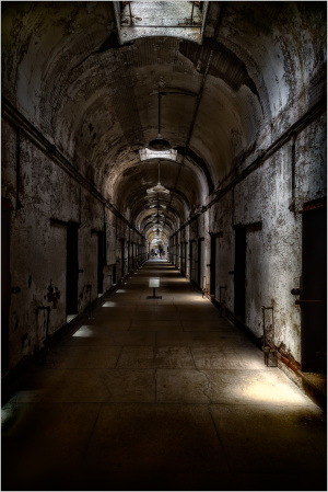 Dimly lit corridor in an old prison with peeling walls and doors on either side