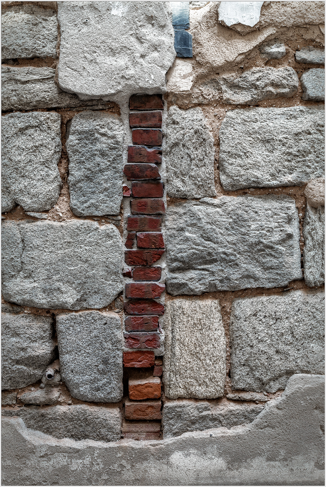 Close-up of a stone wall with a vertical strip of red bricks among gray stones.