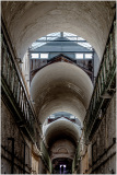 Interior view of a historic prison corridor with arched ceilings and a glass roof.