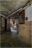 A dimly lit corridor in an old building with peeling walls and a rusty metal box.