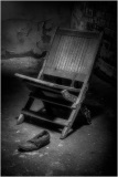 A wooden chair leaning against a wall with a single shoe on the floor nearby.