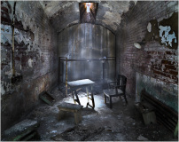 An abandoned room with a table and chair, dimly lit by a shaft of light.