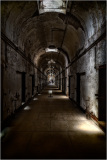 Dimly lit corridor in an old prison with peeling walls and doors on either side