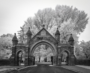 Historic stone archway with towers, leading into a cemetery, surrounded by trees.