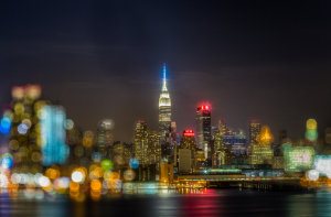 Blurred night view of a city skyline with prominent skyscrapers and illuminated structures.