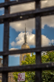 Empire State Building viewed through a metal grid with clouds in the background.