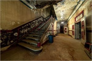Dimly lit hallway with peeling walls and a staircase leading up.