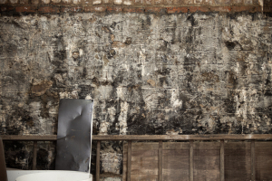 A weathered wall with peeling paint and a lone chair, a stage for shadows and whispers.