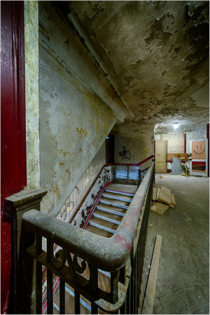 A worn staircase in a dilapidated theater with peeling walls and a dusty floor.