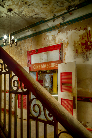 An old theater entrance with red doors and peeling walls, casting shadows in soft light.