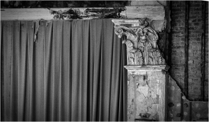 A worn theater curtain and ornate stone column in shades of gray.