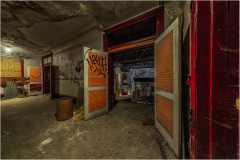 Interior of an abandoned theater with open doors and graffiti on the walls.