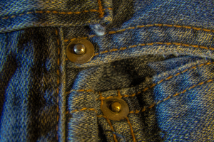 Close-up of worn denim fabric with metal buttons and stitching details.